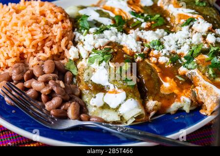 Enchiladas Verdes, oder grüne Enchiladas, mit Huhn gefüllte Tortillas, serviert mit Bohnen und mexikanischem Reis Stockfoto