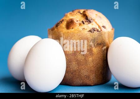 Osterkuchen und drei weiße Hühnereier auf klassischem blauem Hintergrund in der Nahaufnahme. Nahaufnahme von Osterkuchen und Eiern auf einem Stockfoto