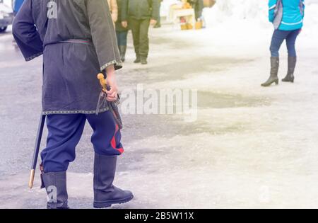 Kosakenpeitsche in der Hand eines Kosakens, der in Nationaltracht, in Kirzov-Stiefeln und mit einem Säbel im Winter auf einer überfüllten Straße geht Stockfoto