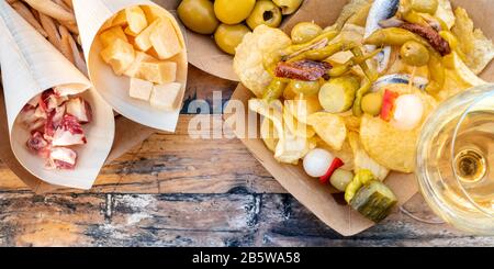 Tapas und Pinchos Panoramaaufnahmen über dem Kopf. Schinken, Käse, Oliven, gildas mit Paprika und Kartoffelchips, mit Weißwein, auf einem Holztisch Stockfoto