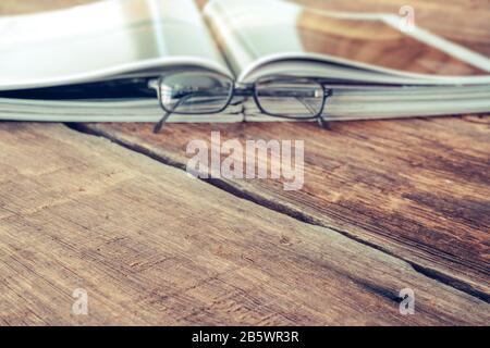 Ansicht der Zeitschrift oder des Katalogs, die mit einer Brille auf dem Holztisch gelesen werden kann. Konzept für Hintergrundtexturen Stockfoto