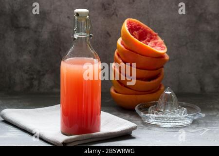 Frisch gepresster Grapefruitsaft in einer Glasflasche, ein Entsafter und Obstschäler auf Betongrund. Stockfoto