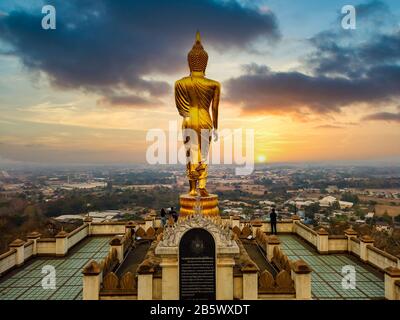 Wat Phra That Khao Noi Temple in Nord-Thailand mit einer großen goldenen stehenden Buddha-Statue, die bei Sonnenaufgang von der Bergkuppe über die Stadt blickt. Stockfoto
