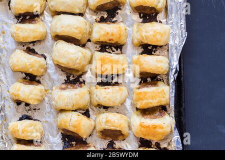 Gebackene Wurstbrötchen auf schwarzem Tisch - Top View Foto von Blätterteig Snacks in Folie gefüttert Zinn auf schwarzer Oberfläche - bereit zum servieren Stockfoto