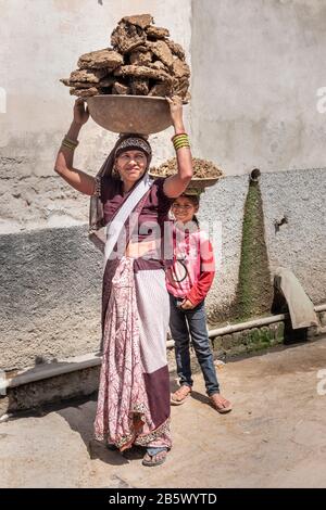 Indianerin und Mädchen, die in Nandgaon ein Becken mit Kuh-Mist-Kuchen auf dem Kopf tragen. Indien Stockfoto