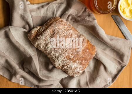 Ganze Laibe mit rustikalem Brot auf Tuch mit Butter und Brotmesser, Foto von oben Stockfoto