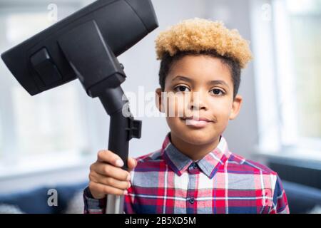 Portrait Of Boy Helfend Out With Chores At Home Holding Vacuum Cleaner Stockfoto