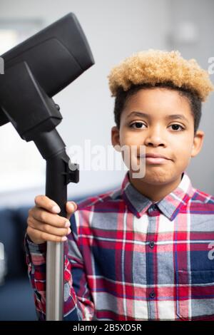 Portrait Of Boy Helfend Out With Chores At Home Holding Vacuum Cleaner Stockfoto