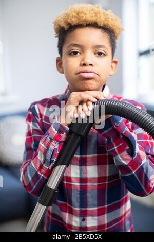 Portrait Des Unglücklichen Jungen, Der Widerwillig Mit Den Chores Bei Home Holding Vacuum Cleaner Hilft Stockfoto