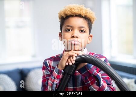 Portrait Des Unglücklichen Jungen, Der Widerwillig Mit Den Chores Bei Home Holding Vacuum Cleaner Hilft Stockfoto