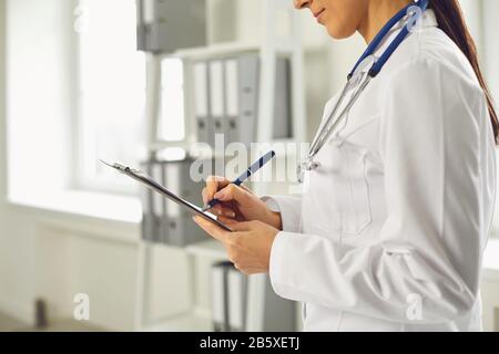 Gesichtslose Ärztin schreibt ein Rezept in die Zwischenablage, während sie im Klinikum steht. Stockfoto