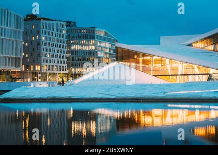 Oslo, Norwegen. Malerische Abendansicht Der Beleuchteten Norwegischen Nationaloper Und Des Balletthauses Unter Modernen Hochhäusern. Stockfoto