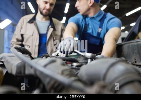 Professioneller Automechaniker plaudert mit seinem Kollegen, während er die Details des Automotors fixiert und mit der Hand fokussiert Stockfoto