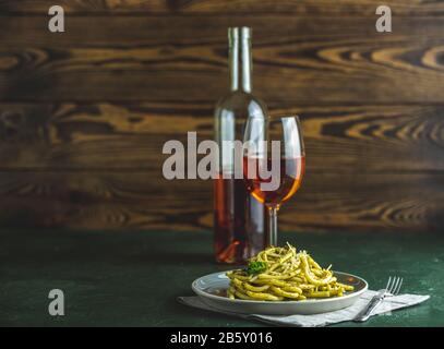 Graue Platte mit Spaghetti-Pasta-Bucatini mit Pesto-Sauce und Parmesan. Traditionelle italienische Perciatelli-Pasta mit genovesischer Pesto-Sauce, serviert mit Wein Stockfoto