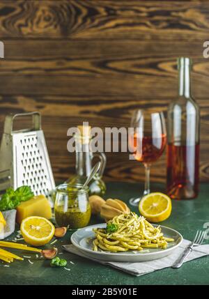 Graue Platte mit Spaghetti-Pasta-Bucatini mit Pesto-Sauce und Parmesan. Traditionelle italienische Perciatelli-Pasta mit genovesischer Pesto-Sauce, serviert mit Wein Stockfoto