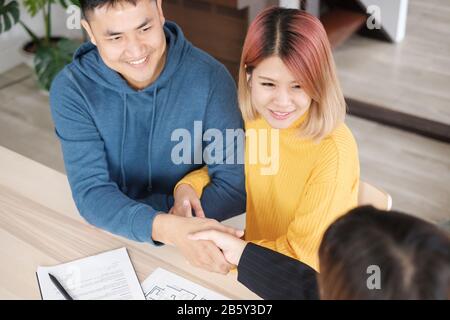 Asiatisches glückliches Paar erhält Schlüssel und Handschlag mit Realtor-Agent mit lächelndem Gesicht in neuem Haus.Kauf neuer Hausimmobilien Stockfoto
