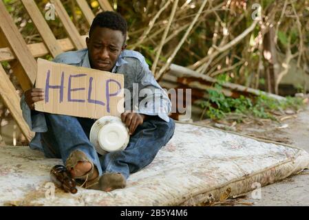 Junger obdachloser Afrikaner mit Pappschild, der um Hilfe bittet Stockfoto