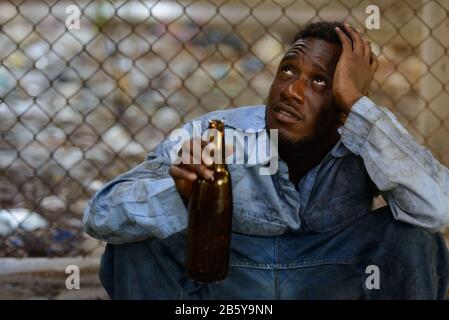 Depressiver junger Obdachloser, afrikanischer Mann, der Bier trinkt Stockfoto