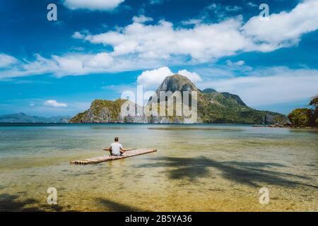 Der Mann, der auf Bambus meditiert, schwimmt umgeben von flachem Lagunenwasser und Inseln der Cadlao-Bucht in einer Entfernung. Palawan, Philippinen. Urlaubsurlaub Stockfoto