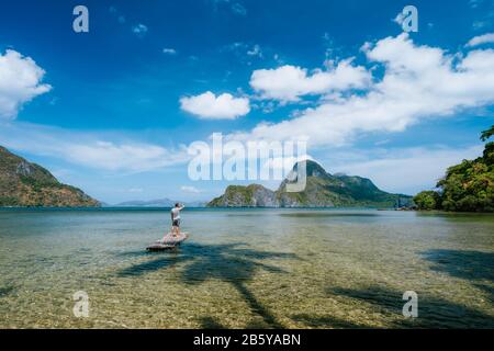 Man auf Bambus schwimmt in einer flachen Lagune mit Panoramablick auf die flache Lagune und die Inseln in der Cadlao-Bucht. Palawan, Philippinen. Urlaubsferienkonzept. Stockfoto