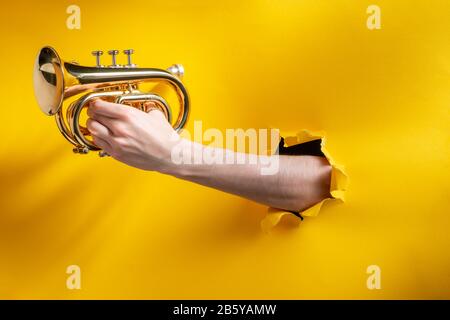 Hand spielt Horn durch zerrissenen gelben Papierhintergrund Stockfoto