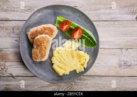 Hühnerschnitzel mit Kartoffelpüree, Tomaten und Salat auf einem runden Teller auf Holzgrund. Draufsicht. Kopierbereich Stockfoto