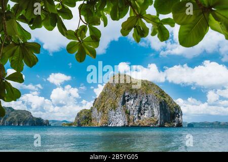 Blätter gerahmt Schuss von der Insel Pinagbuyutan. Blauer Himmel und weiße Wolken im Hintergrund. El Nido, Palawan, Philippinen. Stockfoto