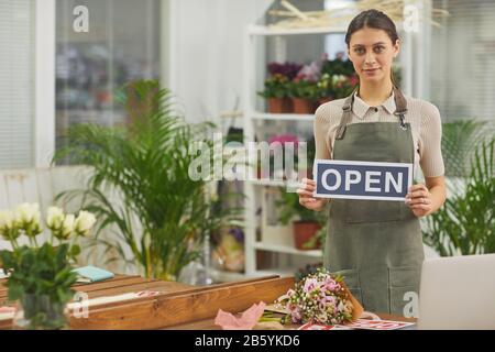 Taille hoch Porträt der lächelnden jungen Frau, die OFFENES Schild hält, während sie in Blumenladen steht, Kopierer Stockfoto