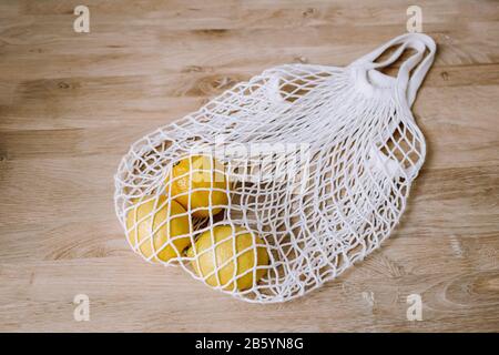 Weiße Saitentasche mit gelben Zitronen auf Holzhintergrund. Öko-Ware für den allgemeinen Gebrauch. Umweltfreundlich, ohne Kunststoff. Draufsicht. Stockfoto