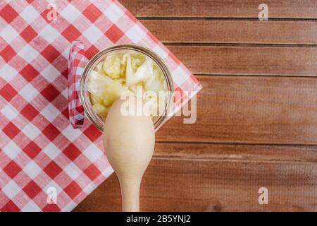 Fermentierter Kohl in einem Glasbecher mit Holzlöffel und Serviette auf Holzgrund. Nahaufnahme. Copyspace. Horizontale Ausrichtung. Stockfoto