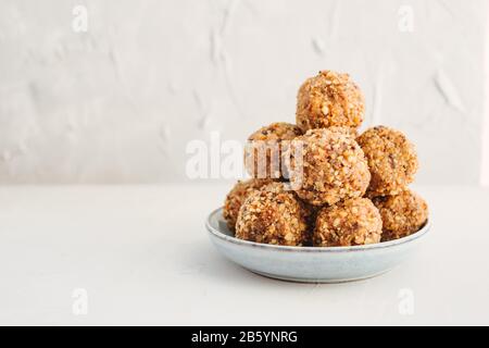 Hausgemachte, gesunde Bioprotein-Energie beißt mit Nüssen, Datteln, Bananen, Kokosöl und Honig. Sportessen, vegetarischer Roh-Snack auf grauem Hintergrund. Stockfoto