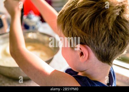 Kleiner Junge, der Pfannkuchen mit Mixer in der Küche zubereitet Stockfoto