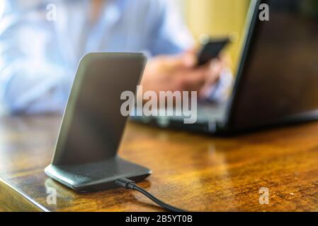 Schnurloses Telefon Ladestation über dem Mann, der das Smartphone zu Hause hält Stockfoto