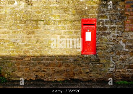 Englische Postbox an Steinmauer im Dorf in england Deutschland Stockfoto