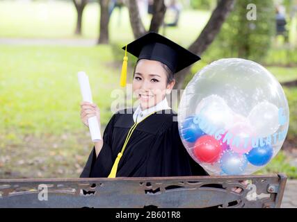 Porträt der glückliche junge Frauen bei den Hochschulabsolventen in den akademischen Kleidung und Square akademischen Cap halten Wort Zitate von CONGRATS Grad auf Ballon nach Einberufung c Stockfoto