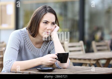 Traurige junge Frau, die auf einer Restaurantterrasse eine Tasse Kaffee schaut Stockfoto