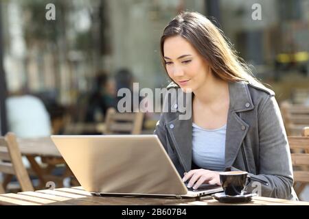 Junge Frau, die ihren Laptop benutzt, sitzt an einem sonnigen Tag auf einer Restaurantterrasse Stockfoto