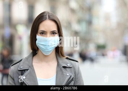 Vorderansicht Porträt einer ernsthaften Frau mit Schutzmaske Vermeidung von Ansteckung Blick auf die Kamera auf der Straße Stockfoto