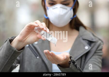 Vorderansicht einer Frau mit Schutzmaske mit Händededesinfektionsmittel zur Vermeidung von Ansteckungen auf der Straße schließen Stockfoto