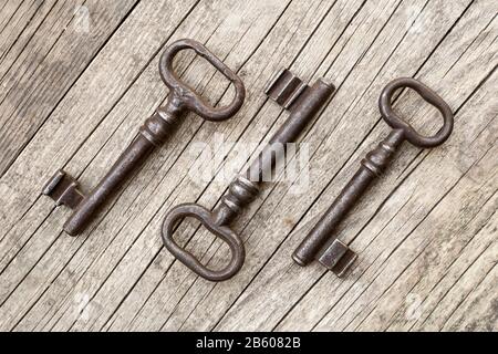 Drei parallele Vintage-Bügelschlüssel auf altem rustikalem Holzhintergrund, Fluchtraumkonzept Stockfoto