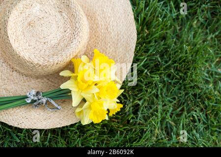 Frühling, Frühling, osterkonzept, Blumenstrauß aus gelben Narzienblumen mit Strohhut im Gras Stockfoto