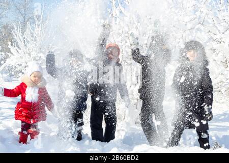Eine Gruppe von Kindern wirft Schnee und genießt die Winterspiele in frischer Frostluft. Hinter ihnen verschneite Bäume. Wunderbarer Winterurlaub. Gesund Stockfoto