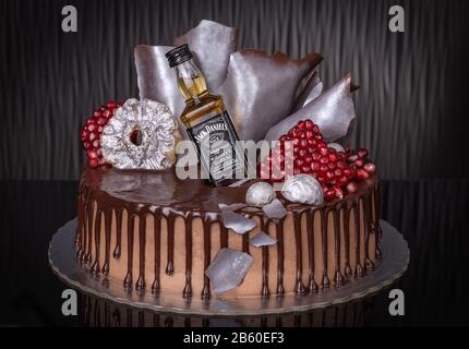 Dekorativer Schokoladenkuchen mit Granatapfel und einer Flasche Whisky. Stockfoto