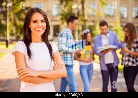 Glückliche erfolgreiche hübsche Frau, die mit ihren Freunden in der Nähe des Campus die Hände überquerte und lächelte Stockfoto