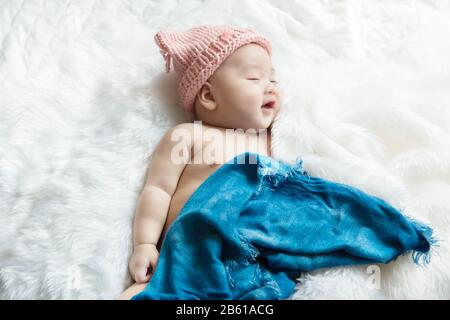 Neugeborenes 30-tägiges Kind lächelt auf seinem weißen Bett und erholt sich unter einem blauen Wickeltuch feelgut glücklich Stockfoto