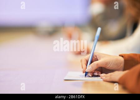 Bild einer menschlichen Hand, die etwas auf dem Papier im Vordergrund schreibt Stockfoto