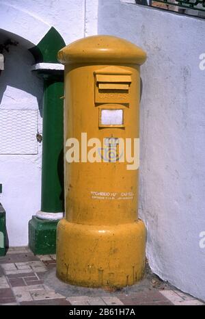 Gelber, bemalter Postkasten/Postkasten gegen eine weiße Wand mit grüner Säule in Competa, Provinz Málaga, Andalucia, Spanien. Stockfoto