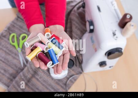 Nähfaden in den Händen einer Näherin. Nähmaschine im Hintergrund. Stockfoto