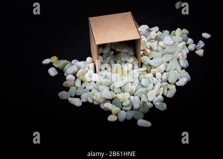 Steinpfirsche graveln um braunen Pappkarton auf schwarzem Grund Stockfoto