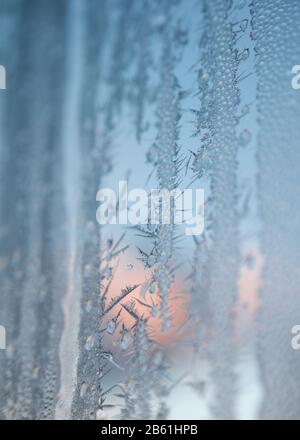 Verhalbauter Winteraufgang durch Fenster, das von Eisblumen bedeckt ist. Wählen Sie Fokus. Stockfoto